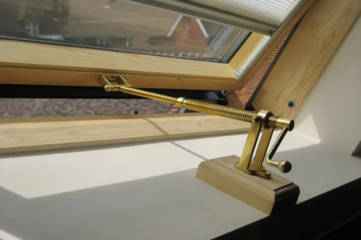 A telescopic screwjack with a handle installed on a pitched roof window
